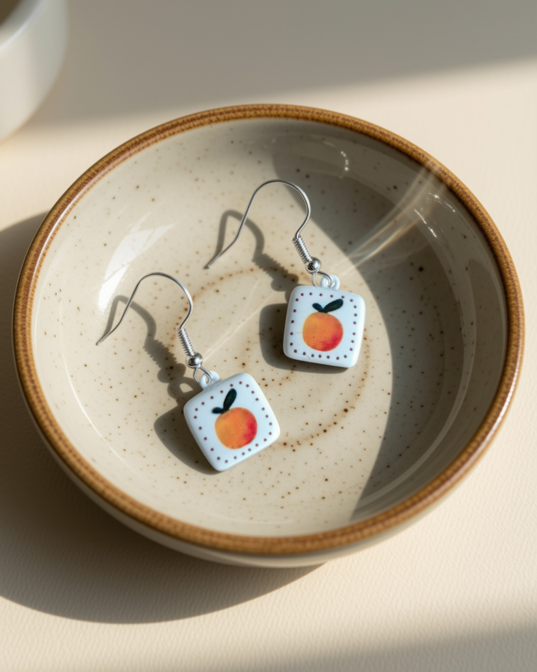 Orange enamel earrings in a ceramic bowl