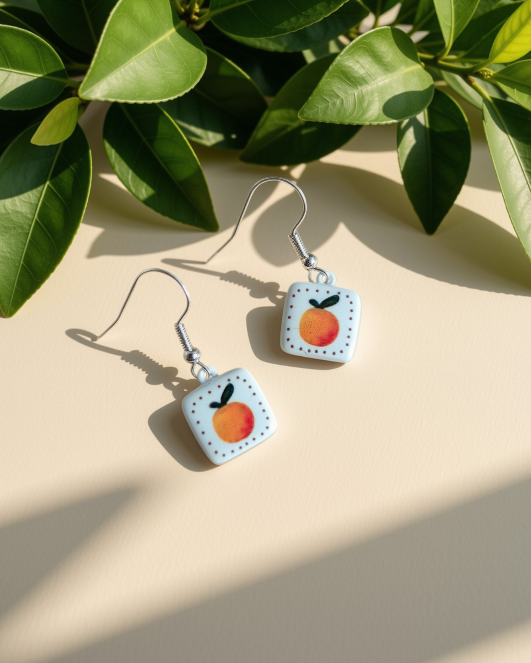 Orange enamel square earrings on green leaves